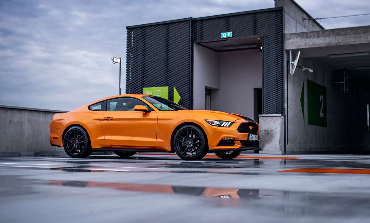 Pomarańczowy Ford Mustang w deszczową pogodę na dachu parkingowym