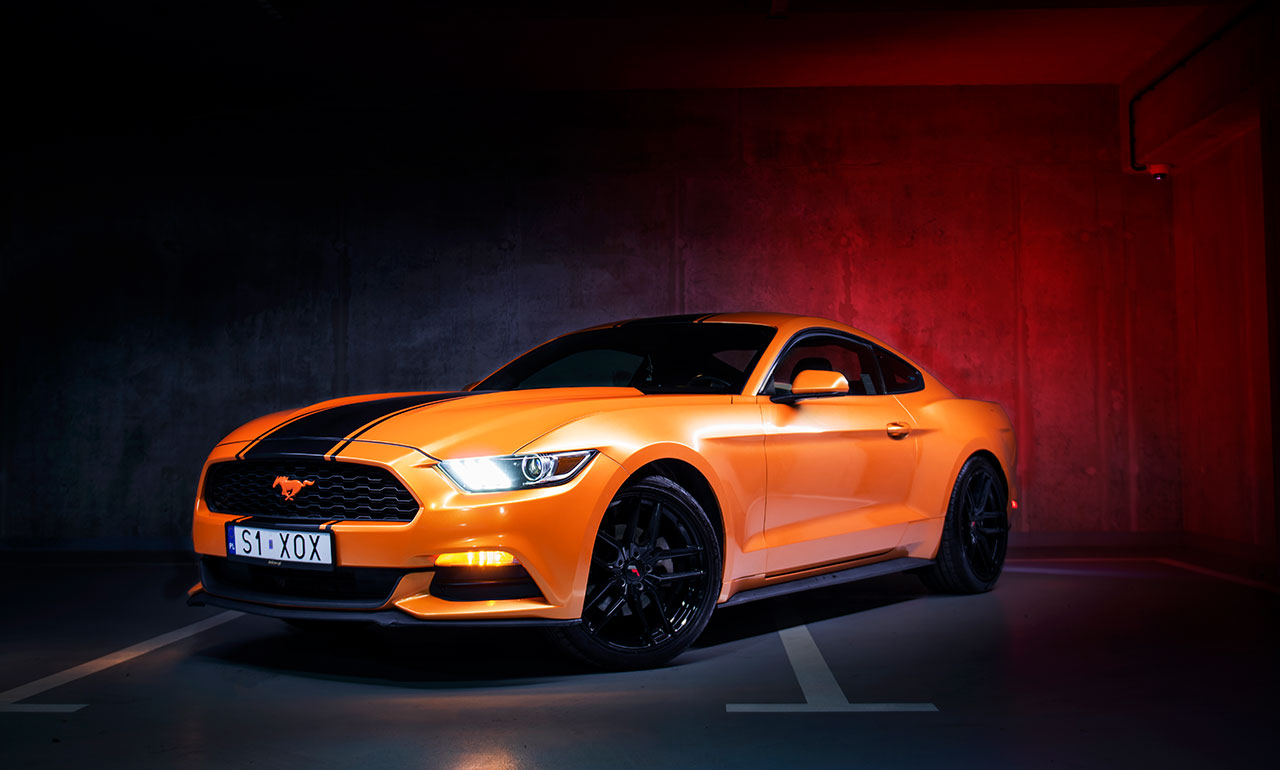 Pomarańczowy Ford Mustang na parkingu podziemnym wśród czerwonej lampy