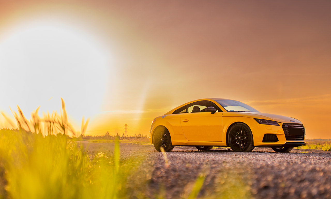sportowe pomarańczowe audi tts na tle zachodzącego słońca, na gruntowej drodze, na łące