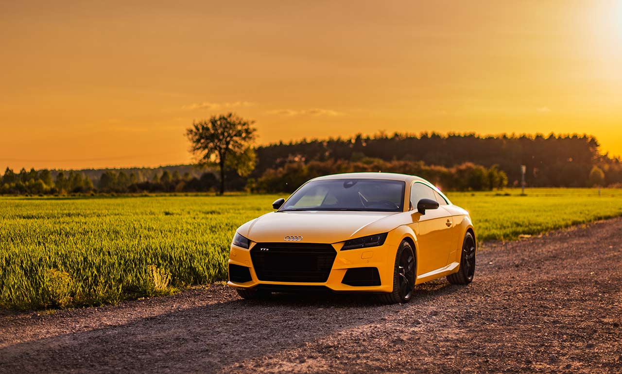 audi tts w kolorze pomarańczowym auto sportowe w dzień zachodzącego słońca w tle pól
