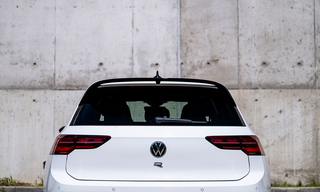 Sportowy Volkswagen Golf 8R w kolorze białym na tle neonowego budynku